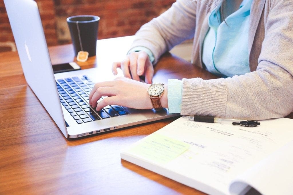 a student typing at a keyboard with coffee and books